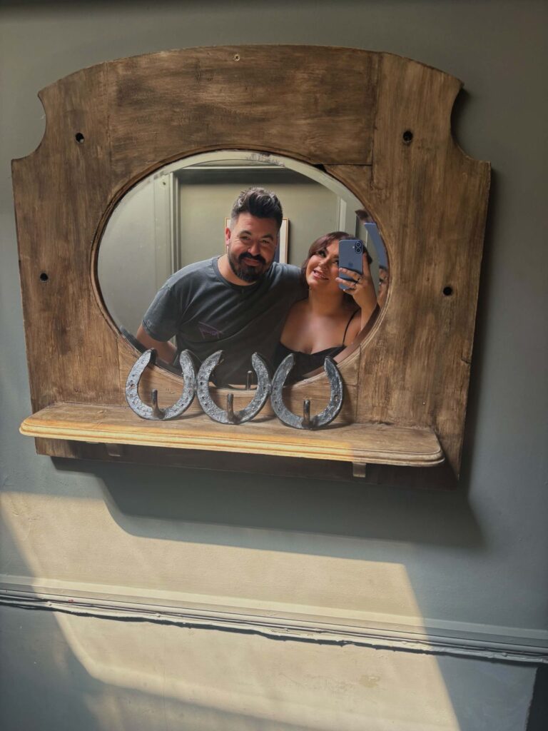 Katie and Alex taking a photograph in the pub mirror, with horseshoes on the shelf below