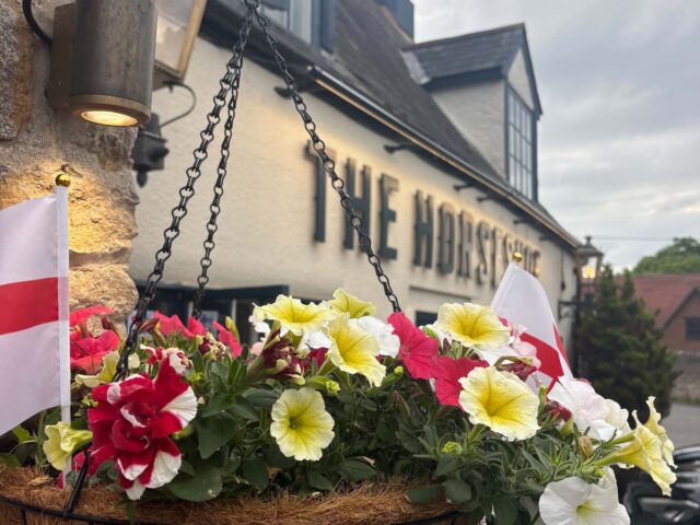 A hanging basket of petunias under THE HORSESHOE on the front