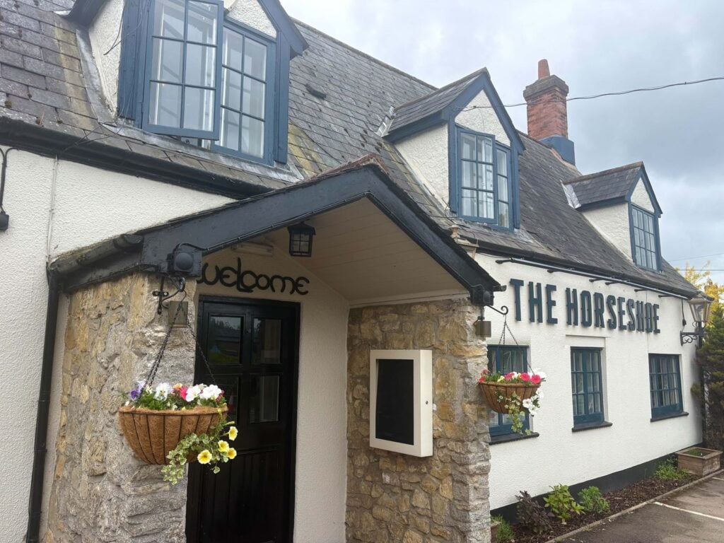 The Horseshoe from the High Street: the stone porch with its Welcome sign, and THE HORSESHOE in dark letters on the white front