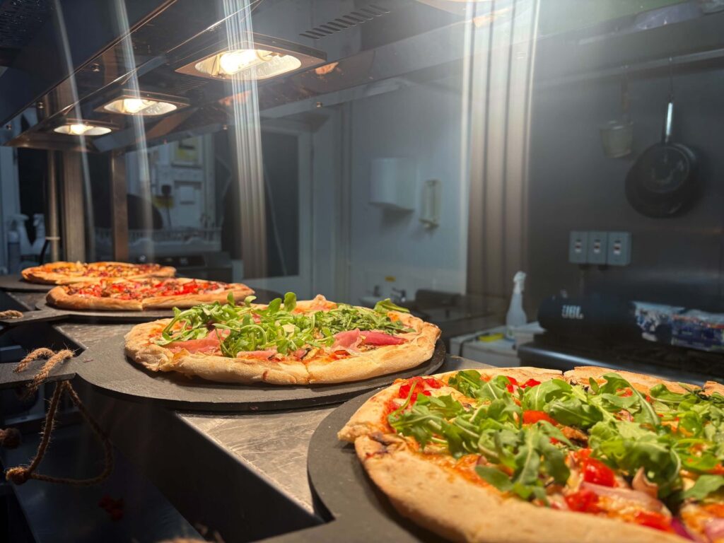 Pizzas lined up under the lights in the kitchen