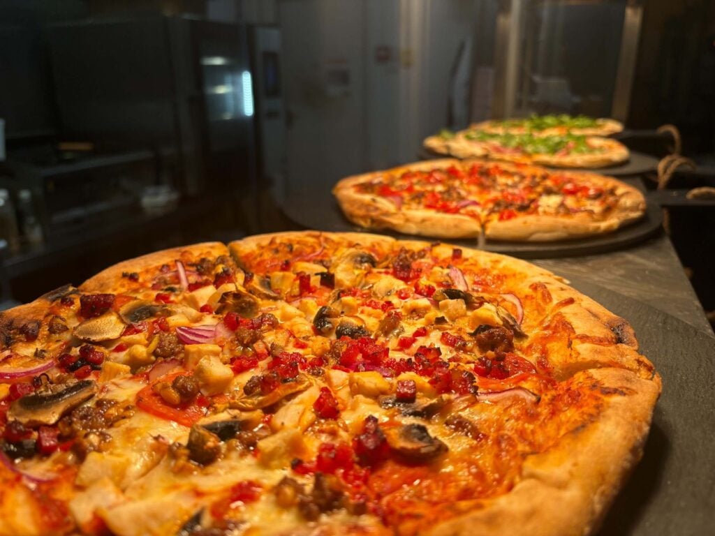 Three sourdough pizzas lined up on the pass in the kitchen