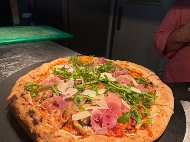A sourdough pizza with prosciutto and rocket on its slate