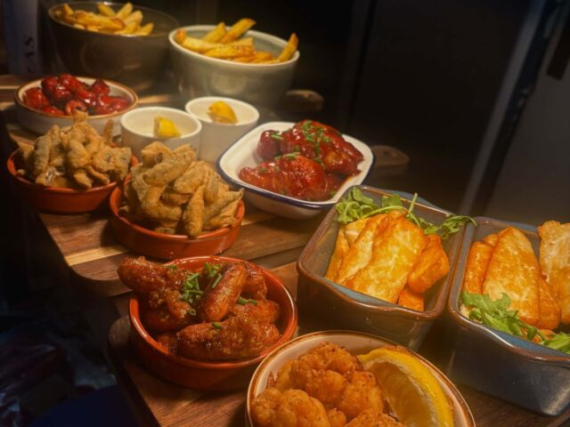 Small plates lined up on the pass: wings, halloumi fries, squid and fries