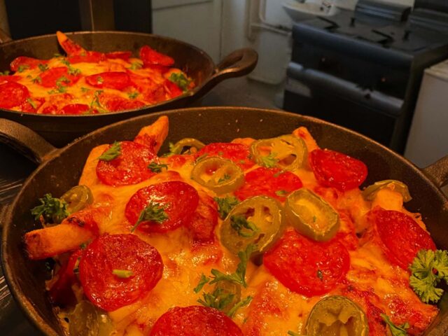 Pizza loaded fries in a pan, with pepperoni and jalapeños
