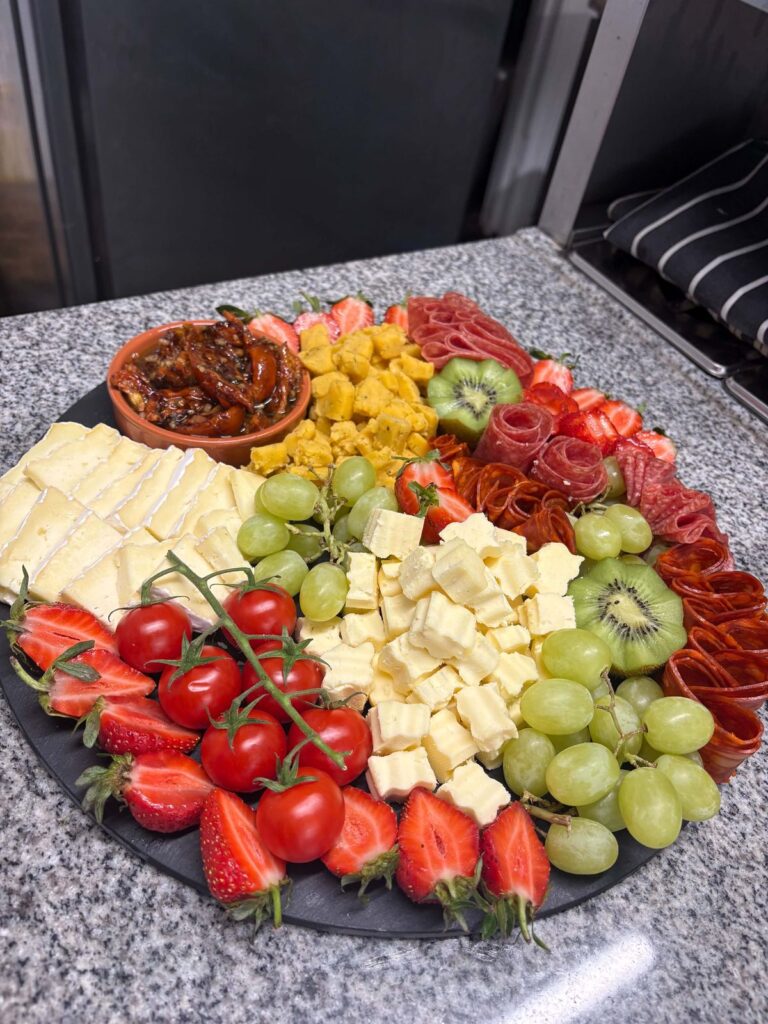 A platter of cheese, strawberries, tomatoes, grapes and kiwi
